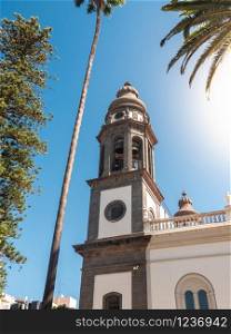 Beautiful photo of high stone catholic church bell tower against blue sky and palm trees. Beautiful image of high stone catholic church bell tower against blue sky and palm trees