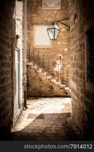 Beautiful photo on narrow street of young woman standing on stone stairs