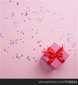 beautiful pink closed box with a big bow on a pink background with multi-colored sparkles, concept of congratulations and surprise, top view
