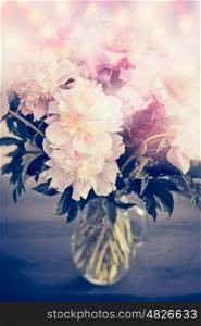 Beautiful pink pale peonies bunch in glass vase on table with bokeh lighting. Romantic flowers bouquet, front view