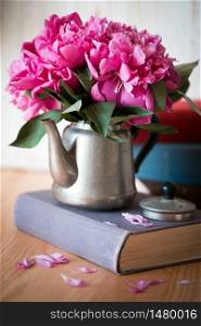 beautiful pink peonies in an old metal teapot for tea standing on a book. wallpaper for smartphone