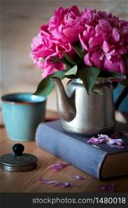 beautiful pink peonies in an old metal teapot for tea standing on a book. wallpaper for smartphone