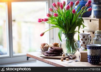 beautiful pink tulips in a vase with cupcakes and cookies in the vintage kitchen. still life