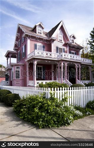 Beautiful pink Victorian house with porch and balcony surrounded by a white picked fence.