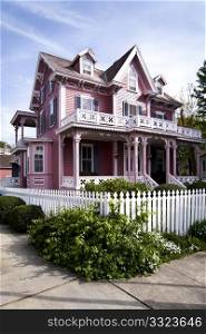 Beautiful pink Victorian house with porch and balcony surrounded by a white picked fence.