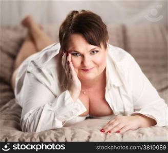 Beautiful plus size woman lying on the bed and looks in the camera, The woman is smiling in a happy manner.