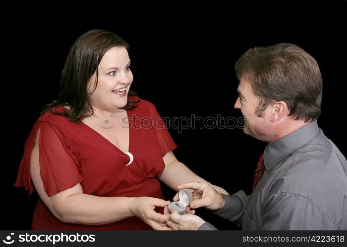 Beautiful plus sized model whose boyfriend is on one knee proposing to her. Black background.
