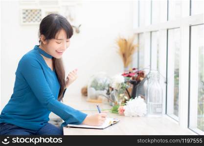 Beautiful portrait asian woman writer excited writing on notebook or diary with happy with success and glad, lifestyle asia girl is student, female plan working, education and business concept.