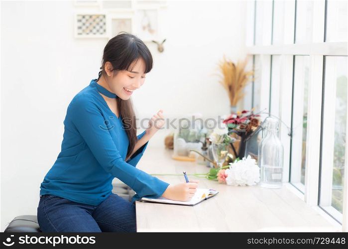 Beautiful portrait asian woman writer excited writing on notebook or diary with happy with success and glad, lifestyle asia girl is student, female plan working, education and business concept.