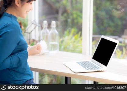 Beautiful portrait asian young freelance woman working online laptop with smile and happy at cafe shop, girl using notebook computer with excited and glad, business and success concept.