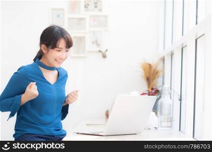 Beautiful portrait asian young freelance woman working online laptop with smile and happy sitting at cafe shop, girl using notebook computer with excited and glad, business and success concept.