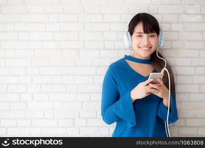 Beautiful portrait asian young woman standing happy enjoy and fun listen music with headphone on cement concrete background, lifestyle of girl relax sound radio with earphone, technology concept.