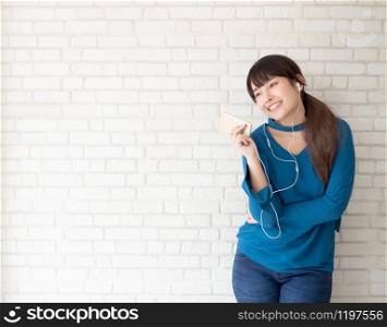 Beautiful portrait asian young woman standing happy enjoy and fun listen music with headphone on cement concrete background, lifestyle of girl relax sound radio with earphone, technology concept.