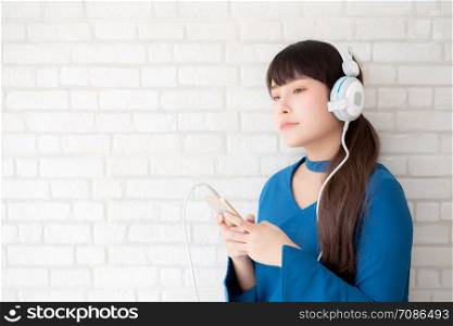 Beautiful portrait asian young woman standing happy enjoy and fun listen music with headphone on cement concrete background, lifestyle of girl relax sound radio with earphone, technology concept.