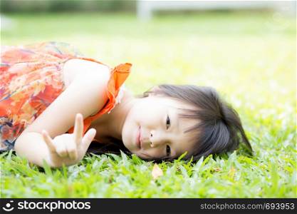 Beautiful portrait little girl asian of a smiling lying on green grass at the park, kid leisure and joyful in outdoor.