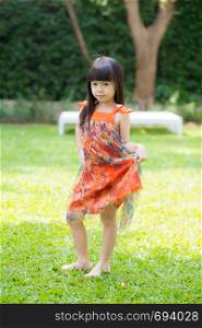 Beautiful portrait little girl asian of a smiling standing on green grass at the park, kid leisure and joyful in outdoor.