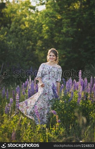 Beautiful portrait of a girl standing in the field of blooming Lupin.. A pregnant girl walks through the blooming lupine field 1683.