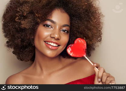 Beautiful portrait of an African girl with a heart shaped lollipop. Valentine’s Day. Symbol of love