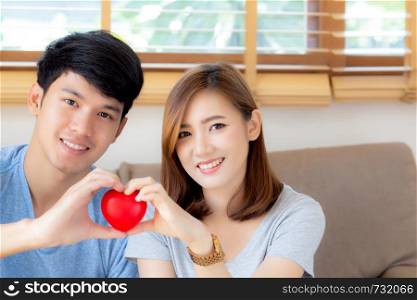 Beautiful portrait young asian couple gesture holding heart shape together, man and woman cheerful smiling and happy sitting on couch, family relationship with love, romantic and sweet concept.