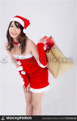 Beautiful portrait young asian woman happy and excited holding paper bag with gift box in xmas holiday isolated on white background, girl shopping and surprise in festive Christmas and new year.