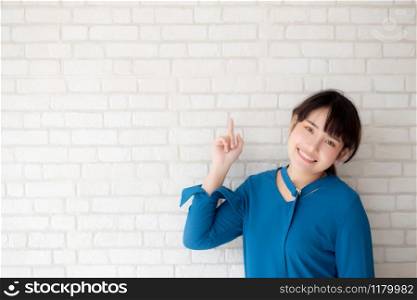 Beautiful portrait young asian woman happy pointing with copy space on cement concrete background, girl smiling standing and showing future or planning with message of you.