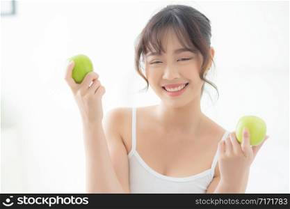 Beautiful portrait young asian woman holding and eating green apple fruit in the bedroom at home, lifestyle of nutrition girl healthy and care weight loss, health and wellness concept.