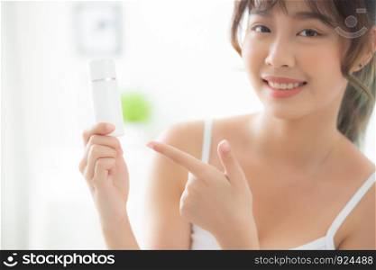 Beautiful portrait young asian woman holding and pointing presenting cream or lotion product, beauty asia girl show cosmetic makeup and moisturizing for skin care, healthy and wellness concept.