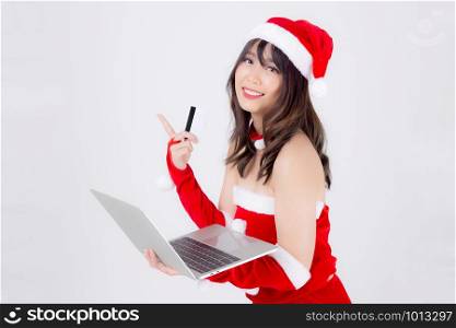 Beautiful portrait young asian woman in Santa holding credit card and laptop computer for shopping online in Christmas holiday isolated on white background, asia girl purchase and pay to internet.