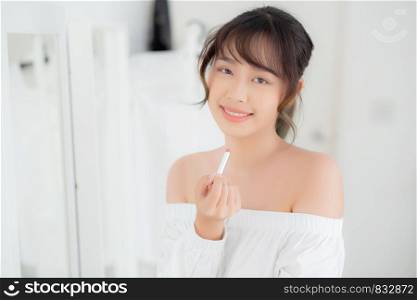 Beautiful portrait young asian woman looking mirror applying makeup lipstick at room, beauty lips asia girl makeup and cosmetic fashion on mouth at home, lifestyle and health care concept.