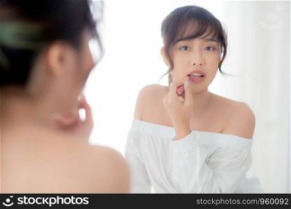 Beautiful portrait young asian woman looking mirror applying makeup lipstick at room, beauty lips asia girl makeup and cosmetic fashion on mouth at home, lifestyle and health care concept.