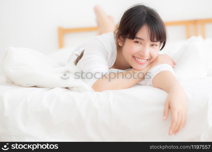 Beautiful portrait young asian woman lying and smile while wake up with sunrise at morning, girl with happy annd fun in the bedroom, lifestyle and relax concept.