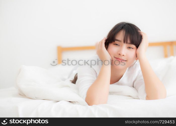 Beautiful portrait young asian woman lying and smile while wake up with sunrise at morning, girl with happy annd fun in the bedroom, lifestyle and relax concept.