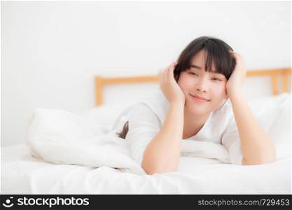 Beautiful portrait young asian woman lying and smile while wake up with sunrise at morning, girl with happy annd fun in the bedroom, lifestyle and relax concept.