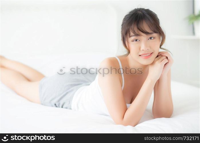 Beautiful portrait young asian woman lying and smile while wake up with sunrise at morning, beauty cute girl happy and cheerful resting on bed in the bedroom, lifestyle and relax concept.