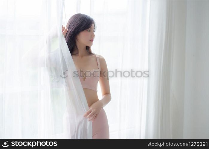Beautiful portrait young asian woman sexy standing the window and smile while wake up with health, body of girl happy with freshness and cheerful with wellbeing, lifestyle and relax concept.