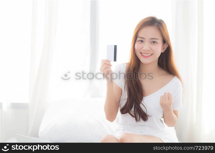 Beautiful portrait young asian woman shopping online with credit card sitting in bedroom, girl with customer purchase of payment online, lifestyle concept.
