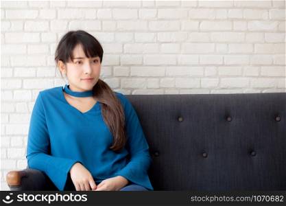 Beautiful portrait young asian woman sitting and smiling happy and looking at camera on sofa with casual at living room, girl cheerful and relax on couch at home, lifestyle concept.
