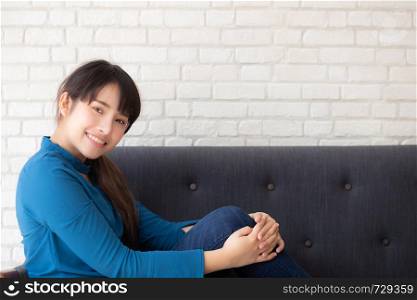 Beautiful portrait young asian woman sitting and smiling happy and looking at camera on sofa with casual at living room, girl cheerful and relax on couch at home, lifestyle concept.