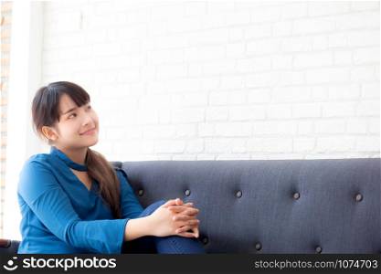 Beautiful portrait young asian woman sitting and smiling happy and looking something on sofa showing future or planning with message of you, girl cheerful and relax on couch at home, lifestyle concept.