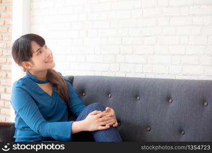 Beautiful portrait young asian woman sitting and smiling happy and looking something on sofa showing future or planning with message of you, girl cheerful and relax on couch at home, lifestyle concept.