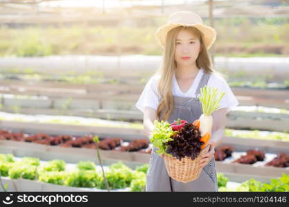 Beautiful portrait young asian woman smile harvest and picking up fresh organic vegetable garden in basket in the hydroponic farm, agriculture and cultivation for healthy food and business concept.