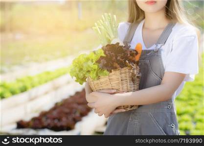 Beautiful portrait young asian woman smile harvest and picking up fresh organic vegetable garden in basket in the hydroponic farm, agriculture and cultivation for healthy food and business concept.
