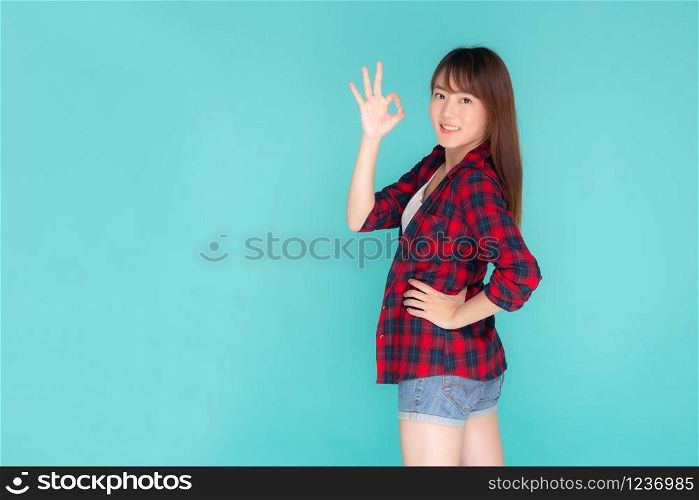 Beautiful portrait young asian woman smiling confident and excited summer holiday isolated blue background, beauty asia model girl gesture ok and cheerful success with journey, travel concept.