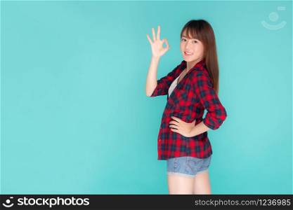 Beautiful portrait young asian woman smiling confident and excited summer holiday isolated blue background, beauty asia model girl gesture ok and cheerful success with journey, travel concept.