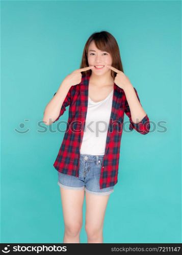 Beautiful portrait young asian woman smiling confident and excited summer holiday isolated blue background, beauty asia girl enjoy and cheerful with pointing cheek journey, travel concept.