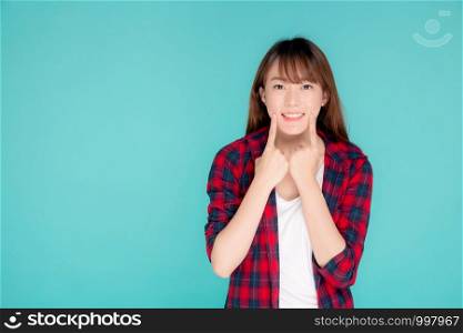 Beautiful portrait young asian woman smiling confident and excited summer holiday isolated blue background, beauty asia girl enjoy and cheerful with pointing cheek journey, travel concept.