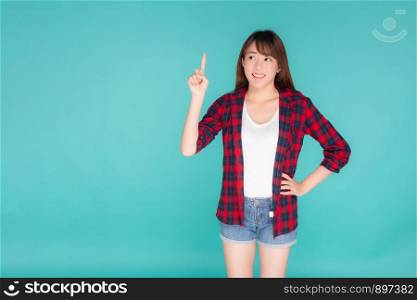 Beautiful portrait young asian woman smiling gesture pointing something and excited summer holiday isolated blue background, asia girl confident and cheerful with journey, travel concept.