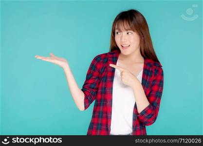 Beautiful portrait young asian woman smiling gesture presenting something and pointing summer holiday isolated blue background, asia girl excited and cheerful with journey, travel concept.