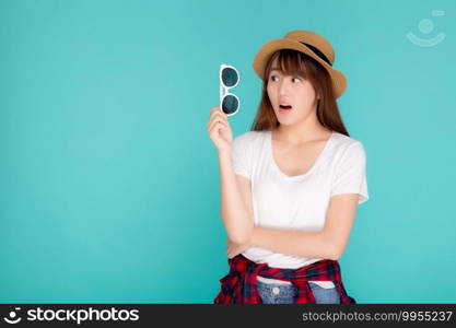 Beautiful portrait young asian woman wear hat and holding sunglasses excited and surprise journey summer trip in vacation isolated on blue background, tourist asia girl amazing with travel.