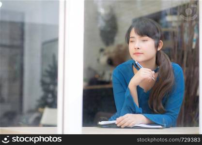Beautiful portrait young asian woman writer smiling thinking idea and writing on notebook or diary with happy, lifestyle of asian girl is student, female planning working, education and business concept.